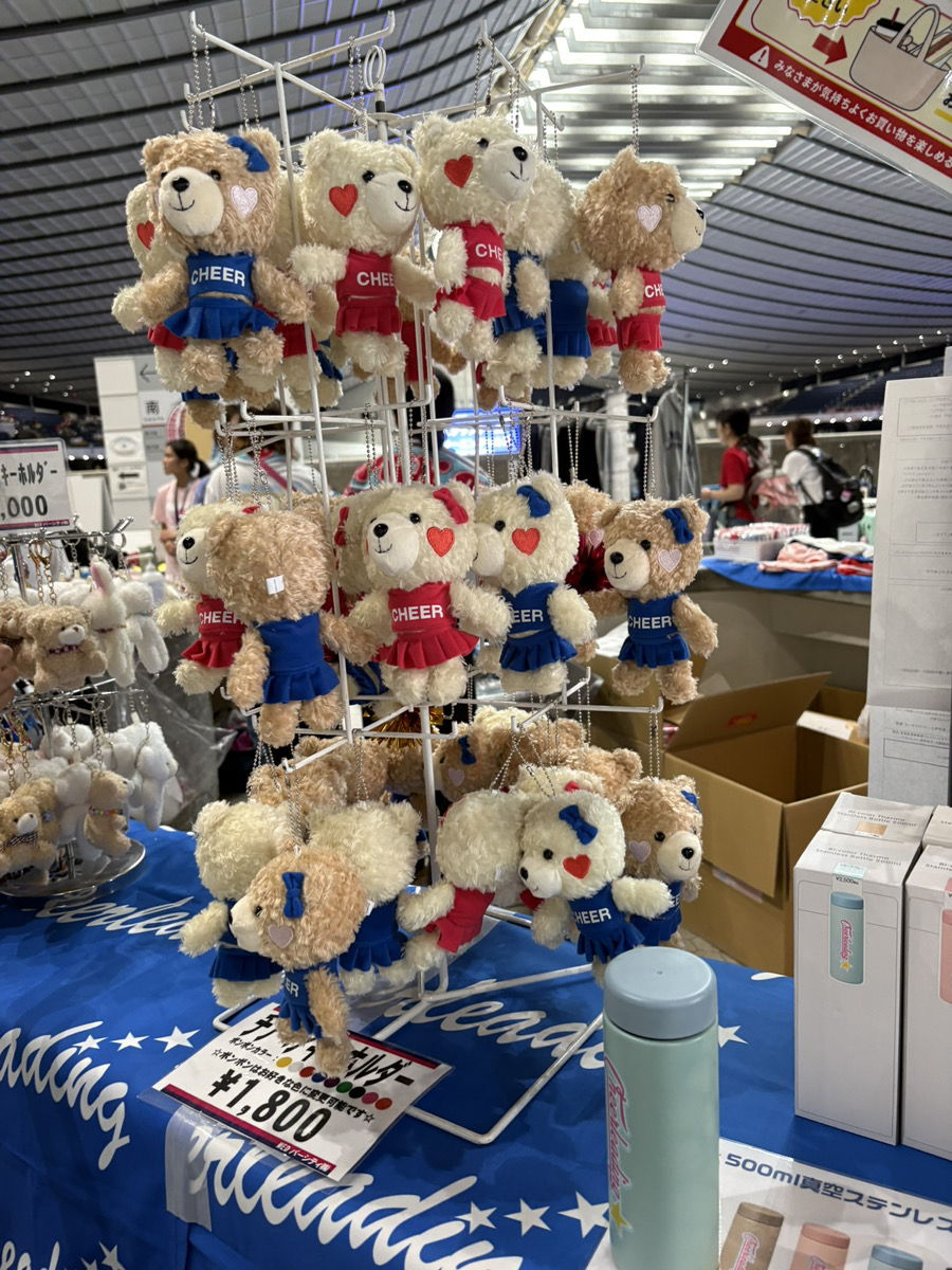 チアユニフォームを着たくまのぬいぐるみキーホルダーが並ぶグッズ売り場