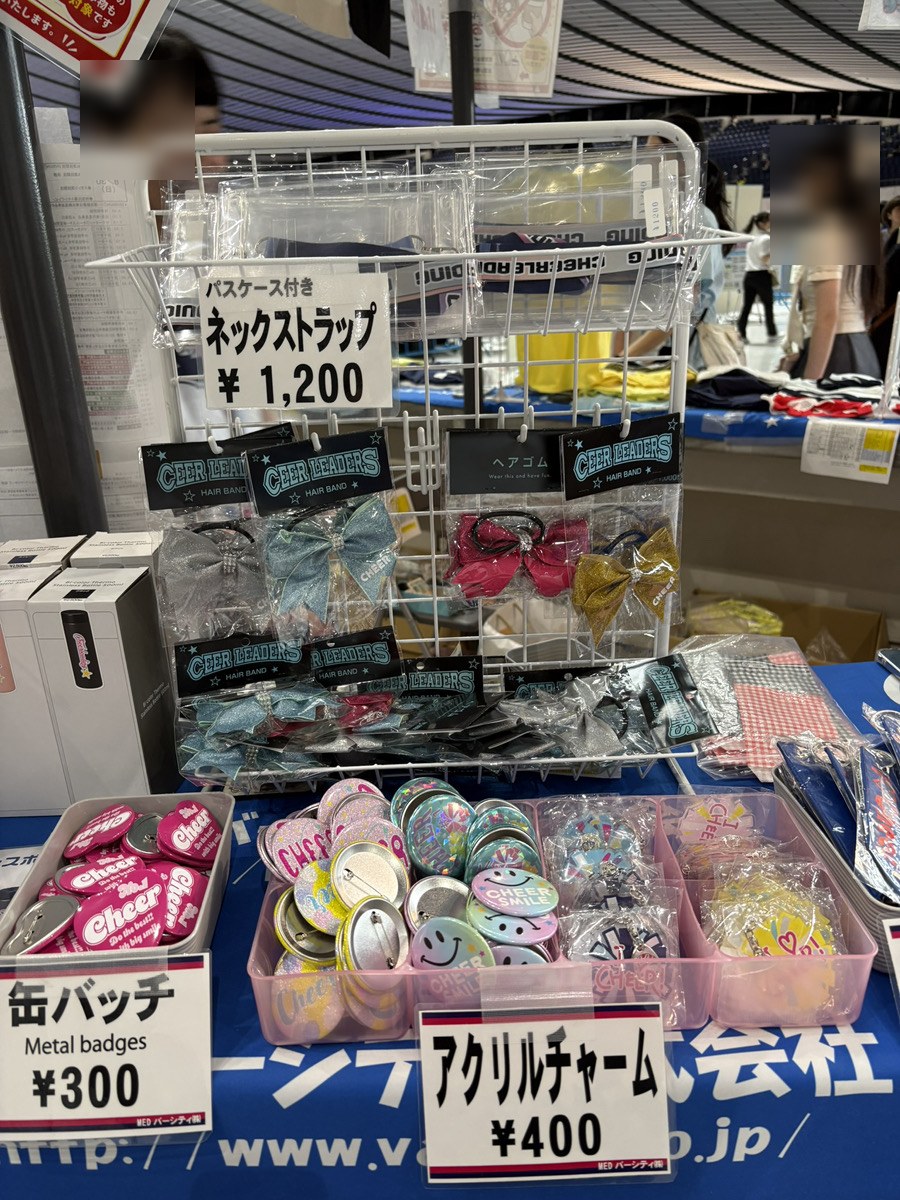グッズ売り場に並ぶ缶バッジ・アクリルチャーム・チア用ヘアリボンとネックストラップ